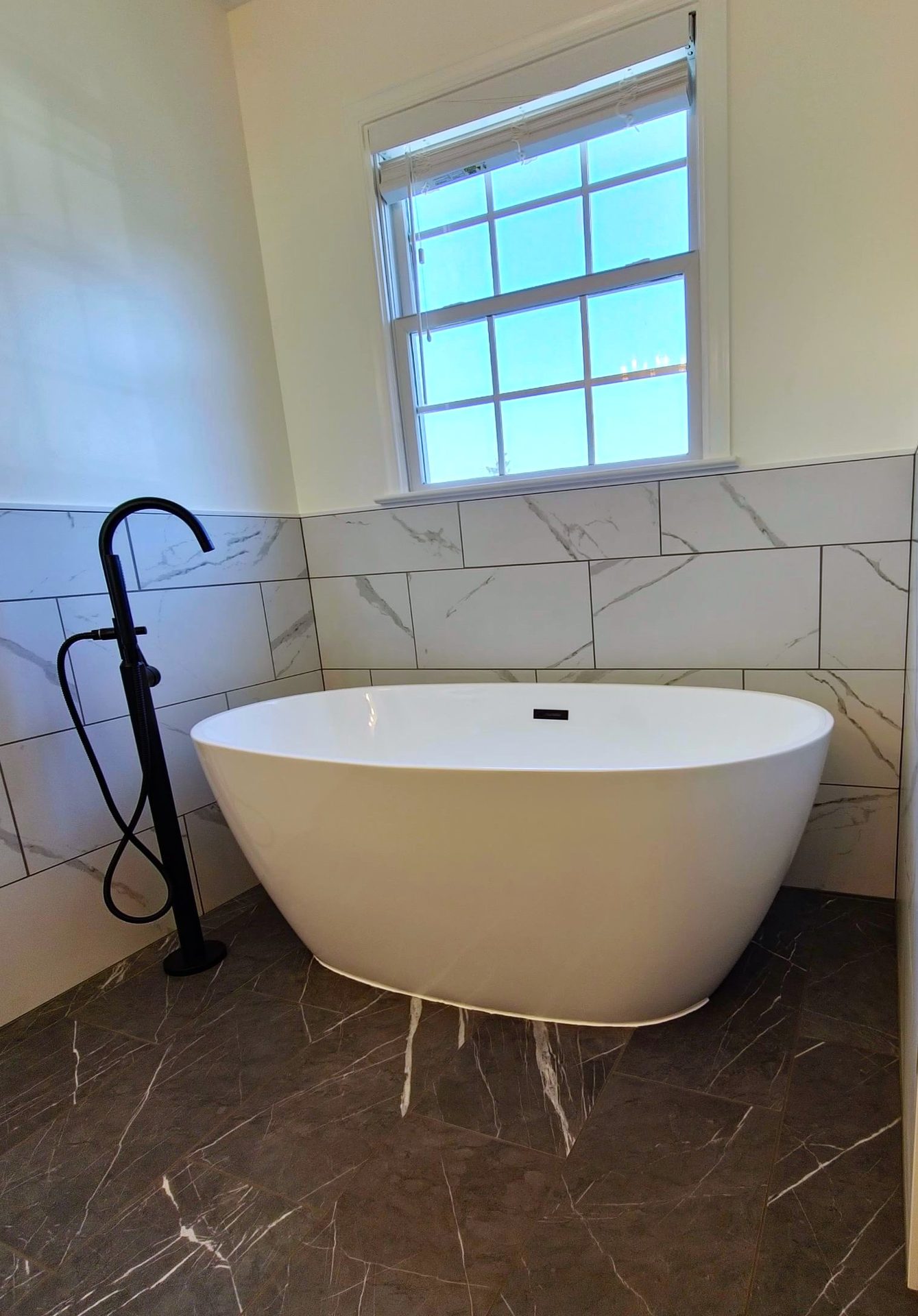 Bowman's Run — freestanding tub against marble-look subway tile with matte black floor-mount filler
