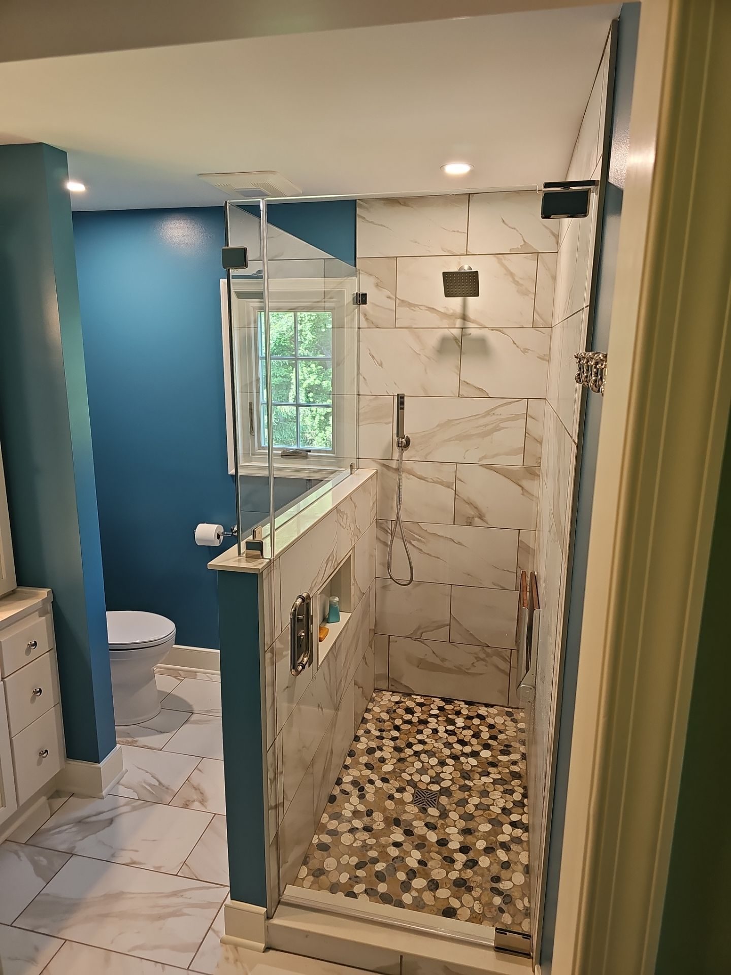 Lime Kiln — walk-in shower with frameless glass, marble-look tile, pebble mosaic floor, and navy walls