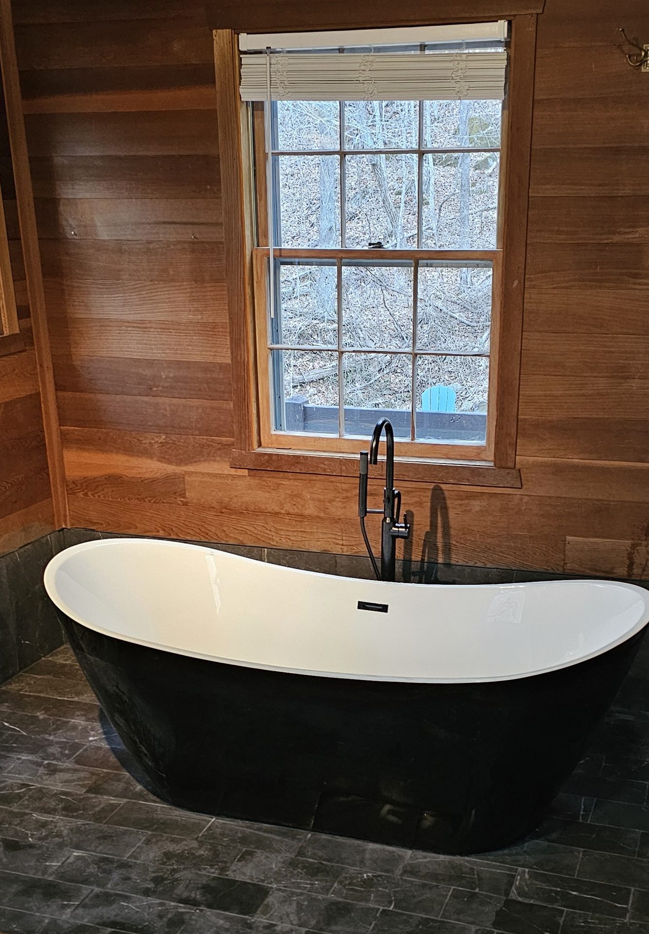 Osceola Mill — freestanding matte-black soaking tub against reclaimed wood paneling with snowy window view